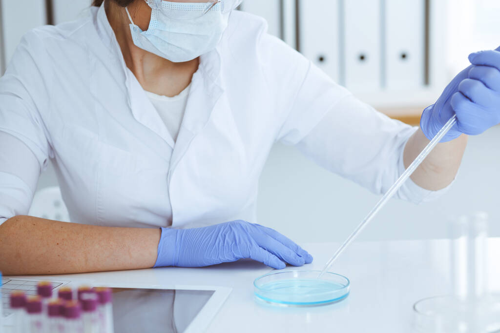 研究室で試薬や血液検査で実験を行う保護眼鏡のプロの女性科学者のクローズアップ.医学、バイオテクノロジー、研究の概念. - 写真・画像