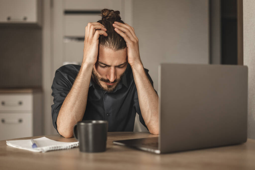 Портрет расстроенного человека с головной болью устал от работы, сидя за столом с ноутбуком - Фото, изображение