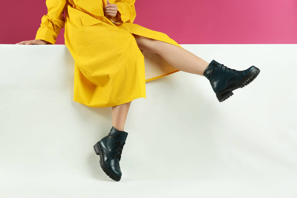 Γυναίκα σε κομψές μπότες κάθεται στο φόντο χρώμα, closeup - Φωτογραφία, εικόνα