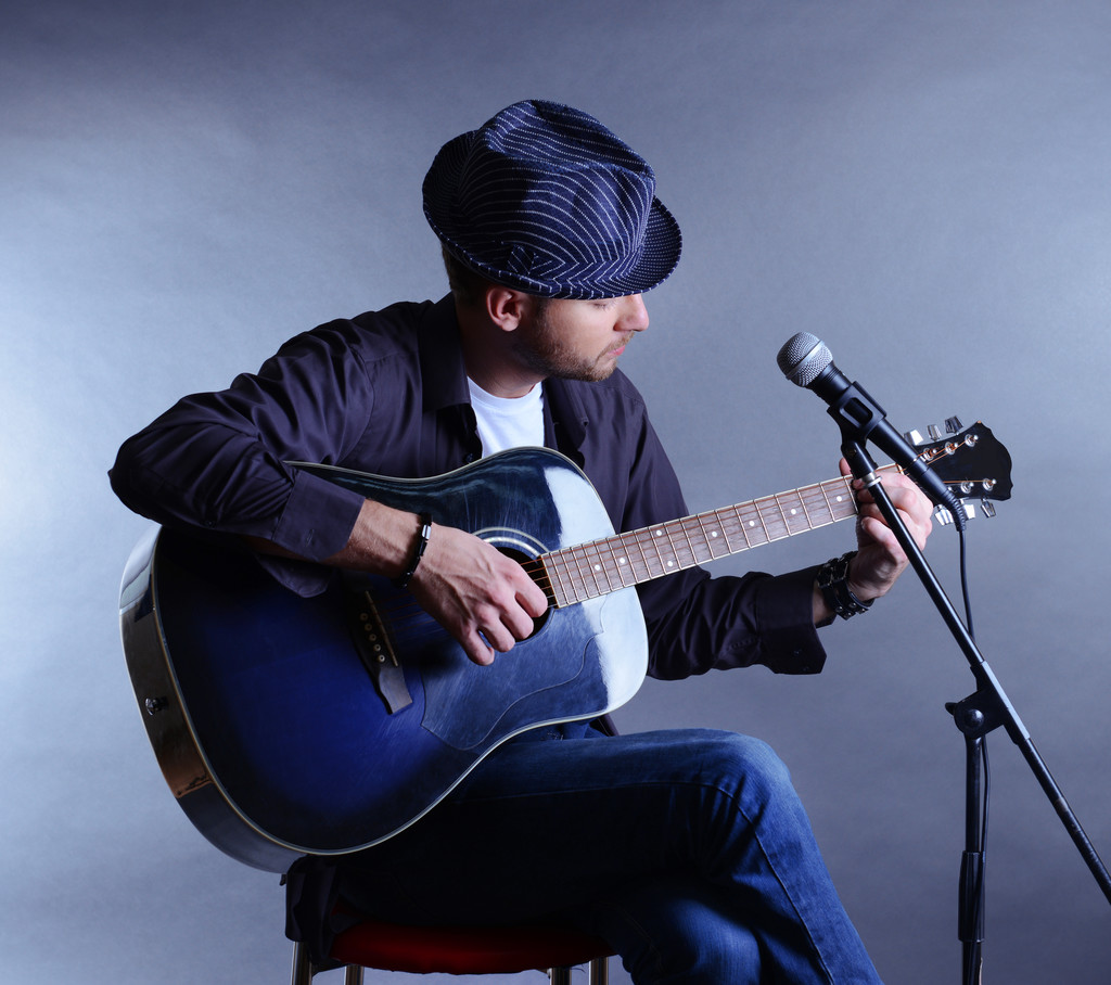 Joven músico tocando guitarra acústica y cantando, sobre fondo gris
 - Foto, Imagen