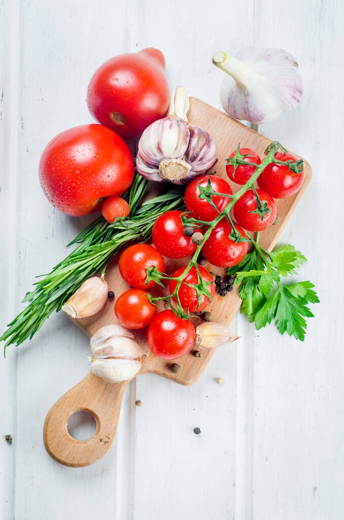 Banda soczystych organicznych pomidorów wiśniowych z zielonym rozmarynem, czosnkiem i przyprawami na białym starym stole. Składniki do gotowania. Czysta koncepcja jedzenia. Dieta wegetariańska. miejsce na tekst - Zdjęcie, obraz