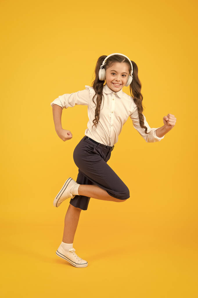 Energetic back to school songs that will get you moving. Energetic child is hurrying to school on yellow background. Small girl enjoying energetic music in earphones. Active and energetic - Photo, Image