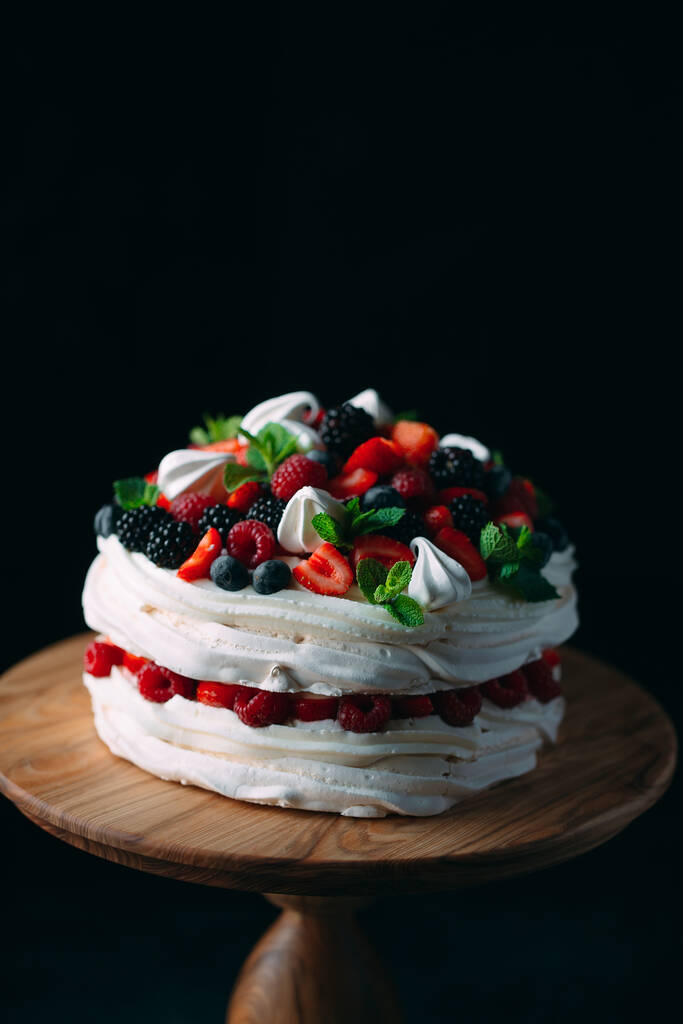 Fruit cake. Cake decorated with berries on a wooden stand on a black background. - Photo, Image