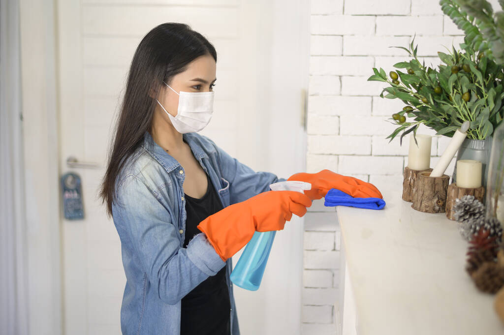 Une femme avec des gants de nettoyage utilisant un désinfectant à pulvérisation d'alcool pour nettoyer la maison, sain et médical, covid-19 concept de protection à la maison . - Photo, image