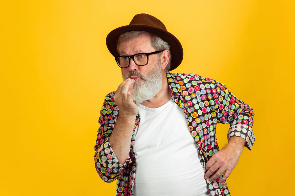 Uomo anziano hipster indossa occhiali in posa su sfondo giallo. Tecnologia e gioioso stile di vita anziano concetto - Foto, immagini