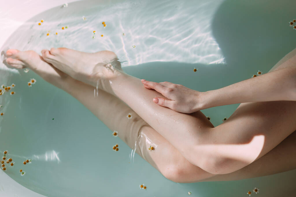 きれいな水と小さな花と浴槽で女性のスリムな足の作物のショット - 写真・画像