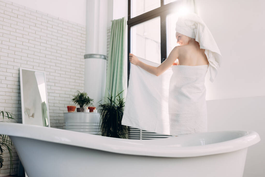 Rudowłosa szczupła kobieta przykrywająca swoje ciało ręcznikiem stojąc w łazience - Zdjęcie, obraz