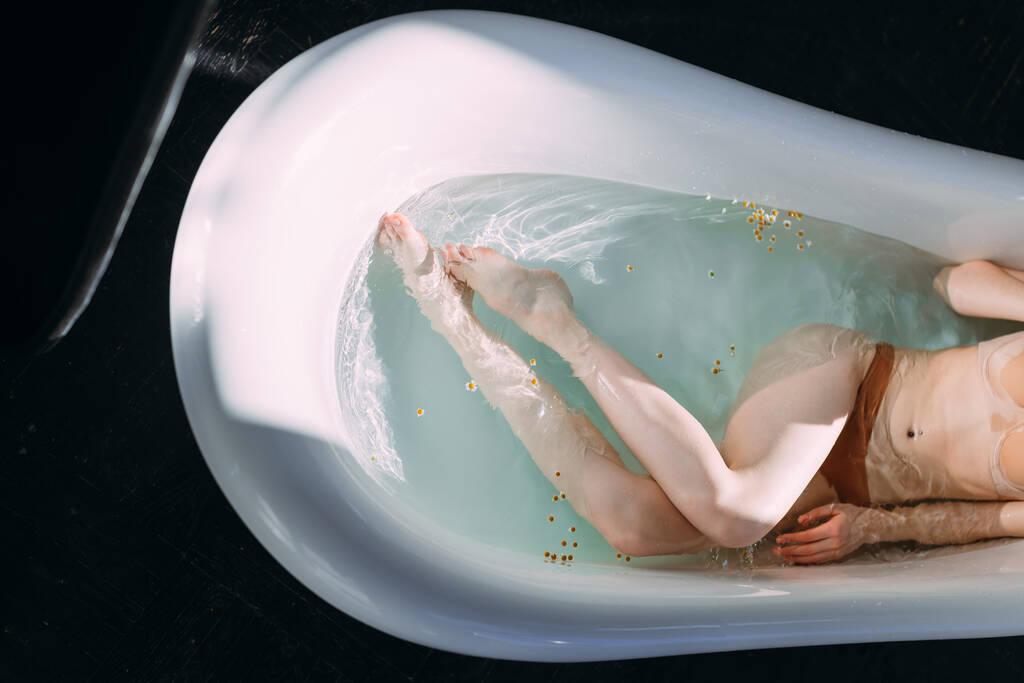 Foto recortada de piernas delgadas femeninas en bañera con agua limpia y pequeñas flores - Foto, imagen