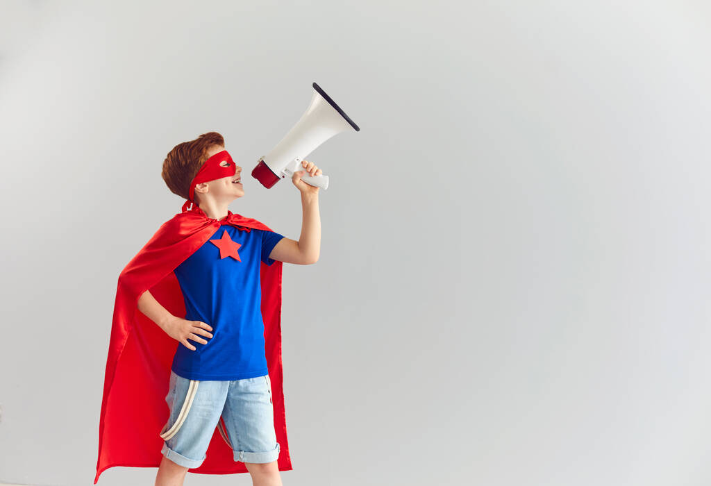 Smiling boy playing role of superhero at home with speaker in hand, copy space - Photo, Image
