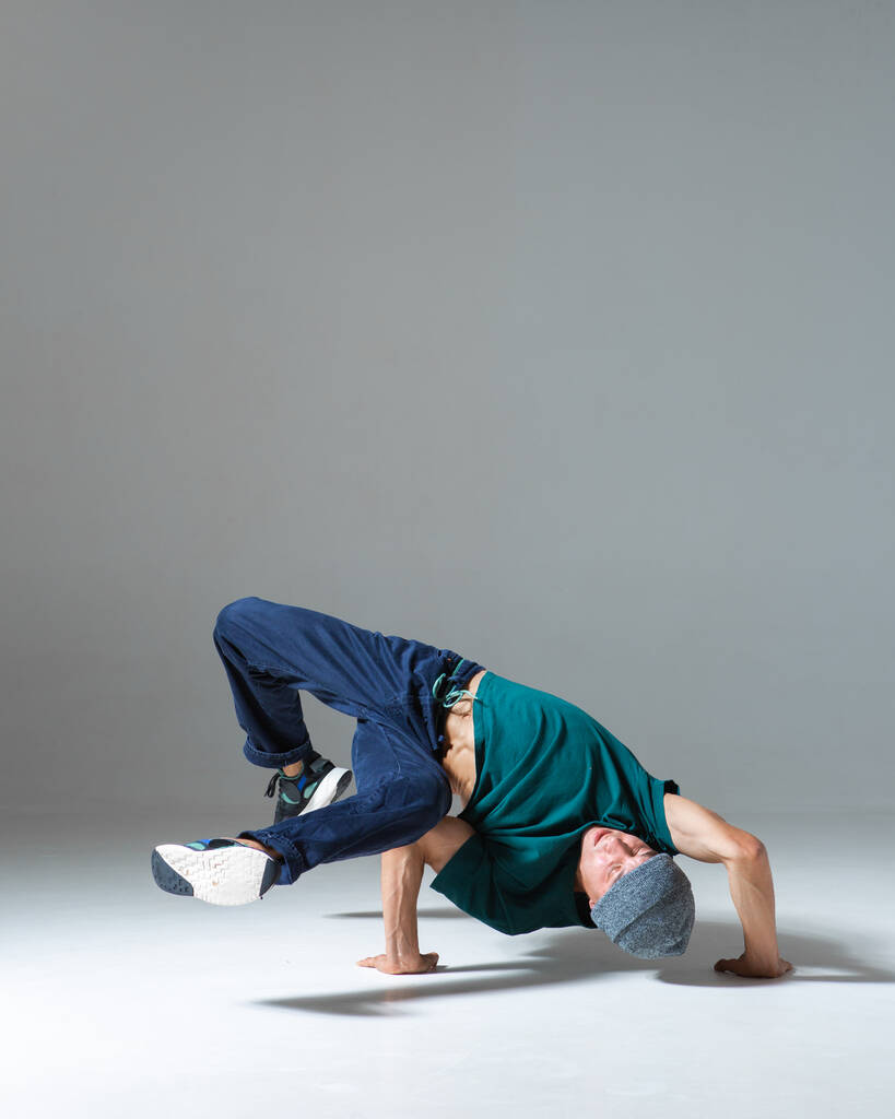 Stylischer junger Mann Breakdancer tanzt Hip-Hop auf dem Boden im Studio isoliert auf grauem Hintergrund. Tanzschulplakat - Foto, Bild