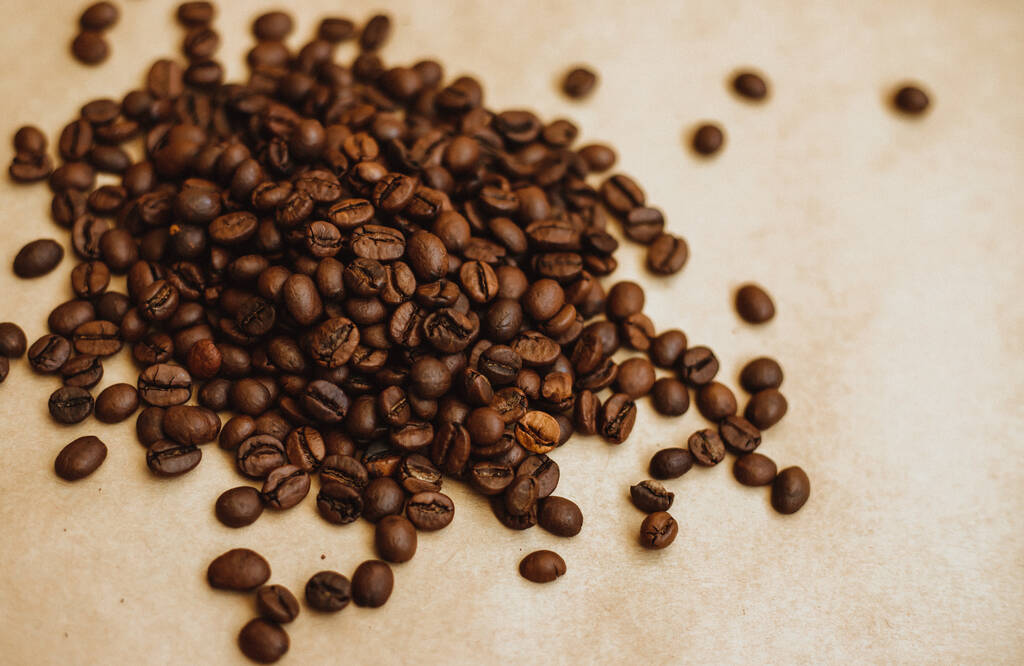 Кофе-бобы фон. Тёмные жареные кофейные зерна, разбросанные по крафт-бумаге. Текстура. - Фото, изображение
