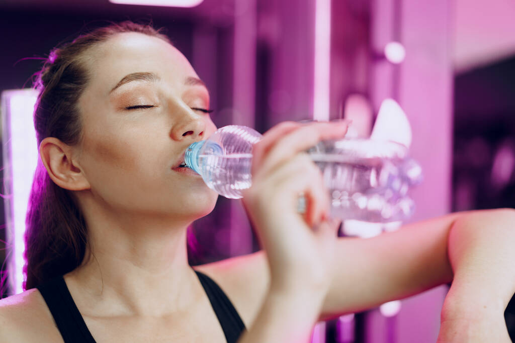 Jonge sportieve vrouw drinkwater in een sportschool - Foto, afbeelding