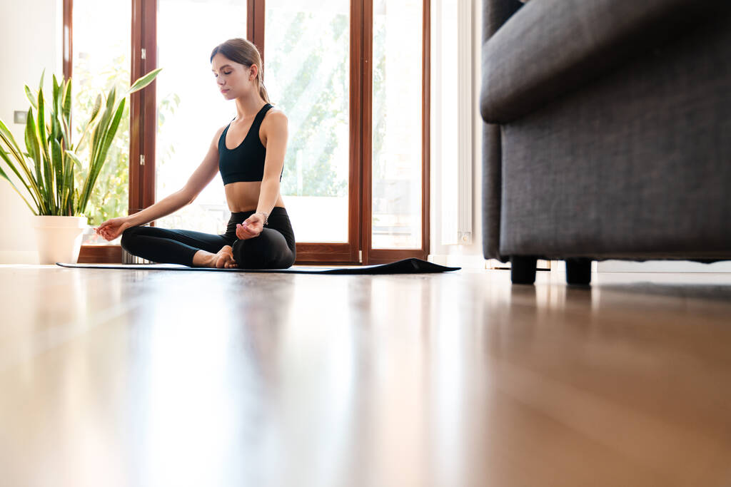 Attrayant jeune femme travaillant à la maison, faire de l'exercice de yoga sur tapis bleu - Photo, image