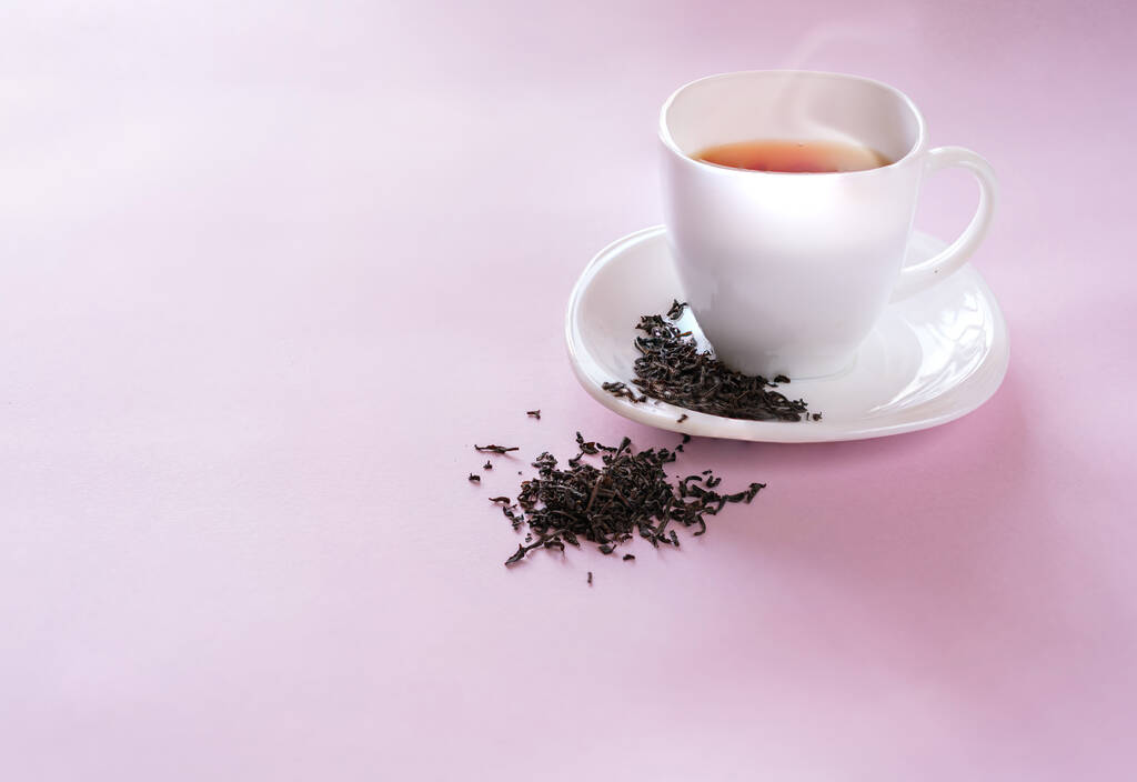 Eine Tasse Tee mit Teeblättern auf rosa Hintergrund. - Foto, Bild