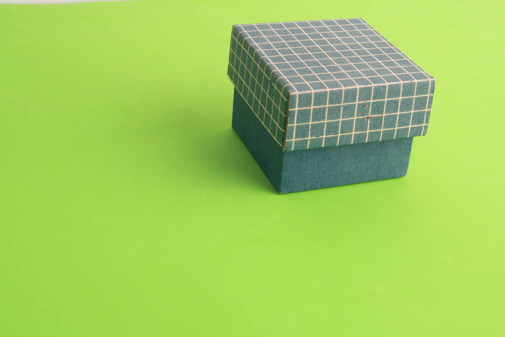 Ένα κοντινό πλάνο από ένα μικρό μπλε χάρτινο κουτί σε πράσινο φόντο - Φωτογραφία, εικόνα