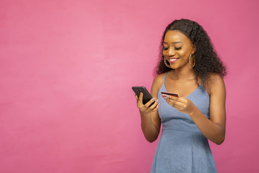 Een mooie jonge Afrikaanse vrouw met behulp van haar mobiele telefoon en creditcard - Foto, afbeelding
