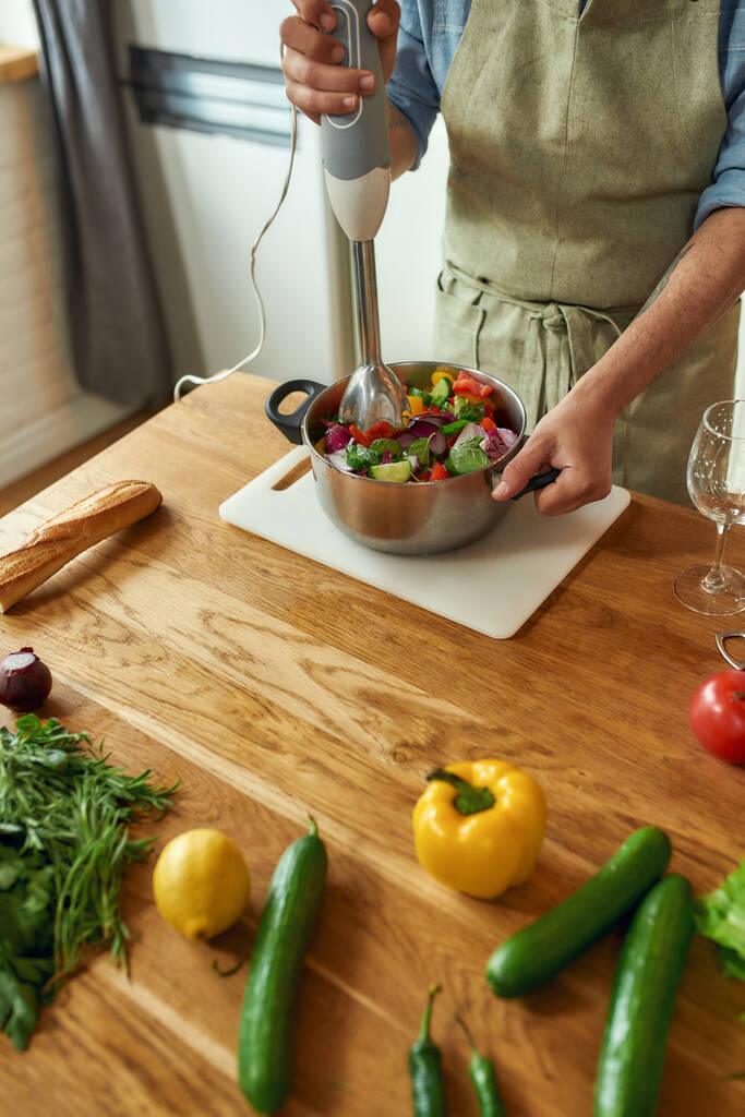 Gehakt shot van de mens, chef-kok met behulp van de hand blender tijdens het bereiden van Italiaanse maaltijd in de keuken - Foto, afbeelding