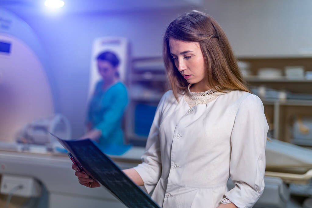 Vrouwelijke arts bespreekt röntgenfoto 's in moderne medische ruimte met computer tomografie. Wazige achtergrond. - Foto, afbeelding