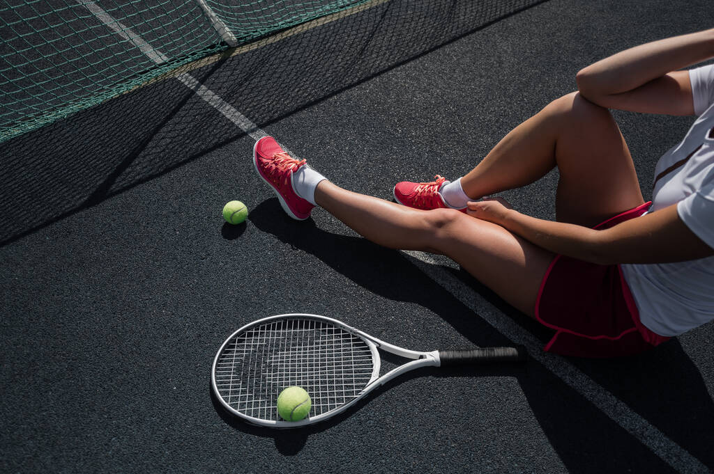 Une fille sans visage en jupe de sport s'assoit sur un court de tennis et tient une fusée. Vue du dessus des jambes féminines. - Photo, image
