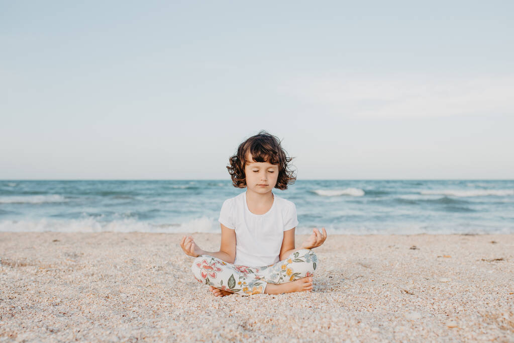 Gyermek lány ül a strandon meditál, jógázik, lazít figyelmes légzés - Fotó, kép