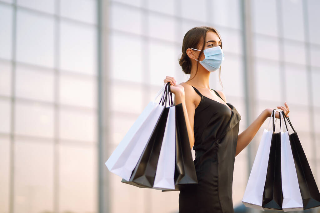 Прекрасна жінка в захисній стерильній медичній масці з сумками для покупок біля торгового центру. Купівля, чорна п'ятниця, продаж концепції. Covid- 2019. - Фото, зображення