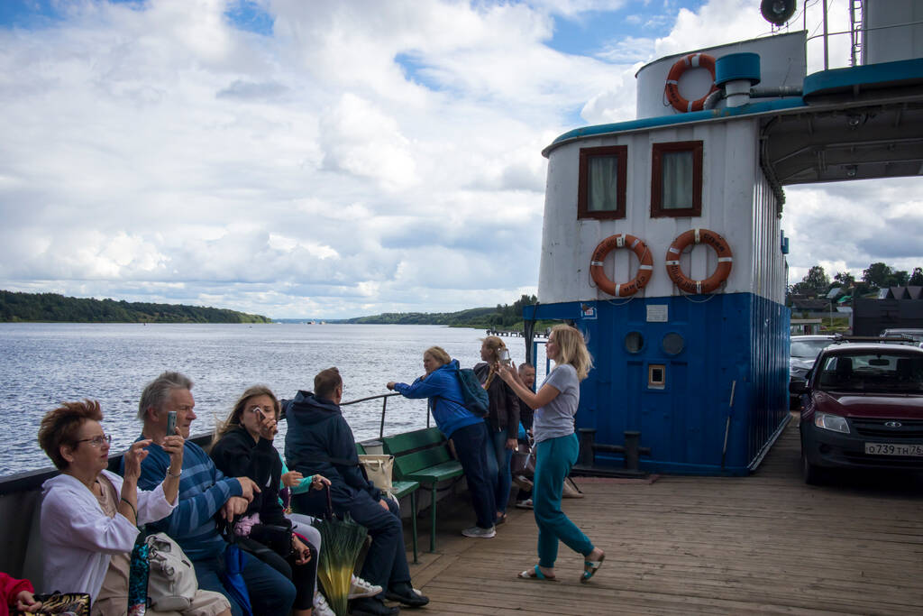 Tutaev, Rússia - 16 de julho de 2029 Paisagem do Volga com uma alta margem oposta com uma igreja branca. Pessoas no ferry ao lado do ferry através do rio largo em primeiro plano - Foto, Imagem
