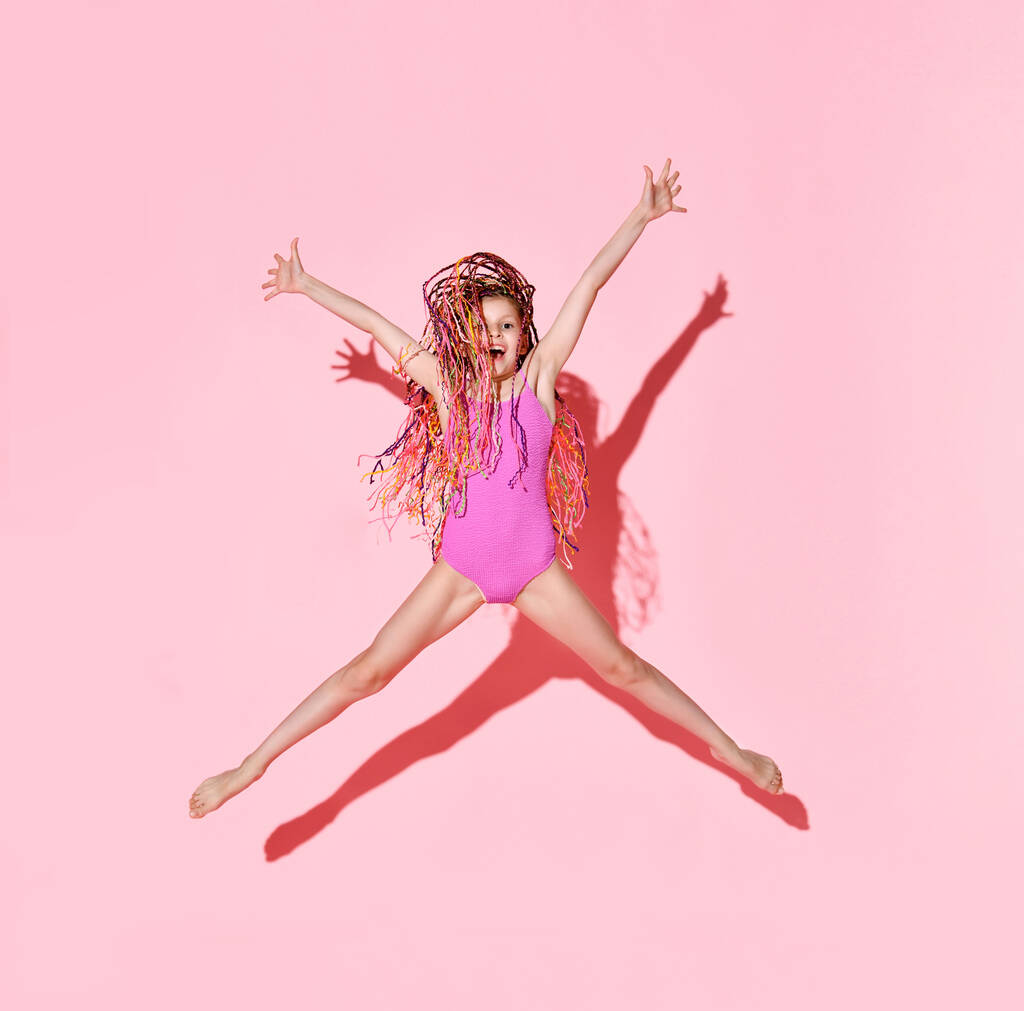 Usmívající se šťastná holčička v plavkách skáče na růžovém pozadí. - Fotografie, Obrázek