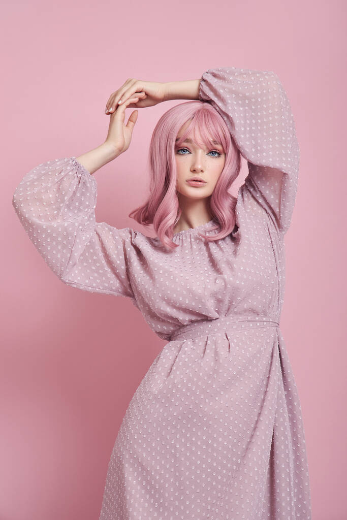 Жінка з пофарбованим рожевим волоссям у довгій сукні. Портрет дівчини з забарвленням волосся на рожевій стіні. Ідеальна зачіска і укладання волосся
 - Фото, зображення