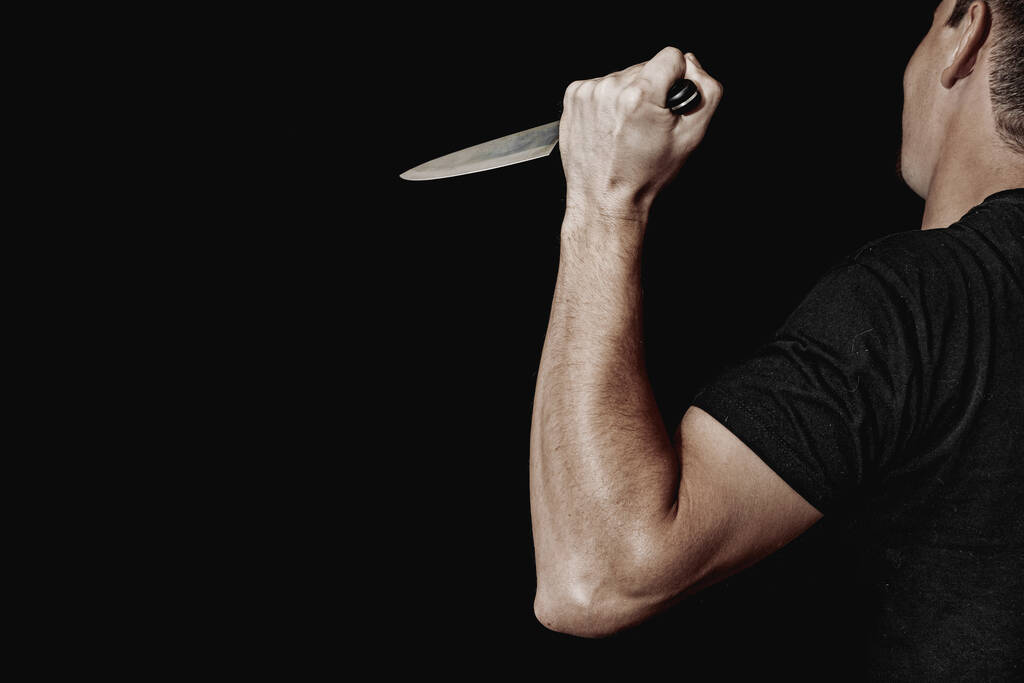 Το χέρι του ανθρώπου κρατάει μαχαίρι σε μαύρο φόντο. θέματα βίας και δολοφονίας. κλέφτης, δολοφόνος, βιαστής, μανιακός - Φωτογραφία, εικόνα