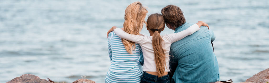 Panoramatický záběr dívky objímající rodiče na pláži v blízkosti moře  - Fotografie, Obrázek