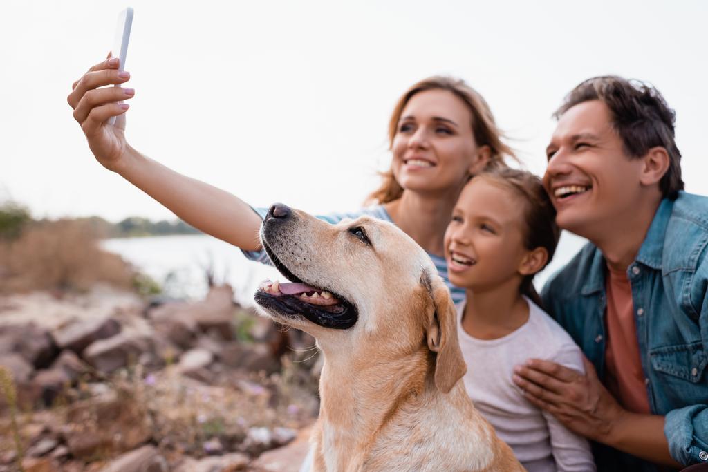 Enfoque selectivo de la familia con golden retriever tomando selfie en smartphone en la playa  - Foto, imagen