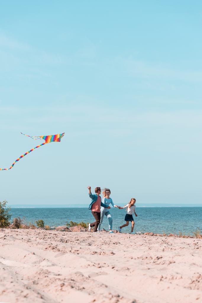 Concentration sélective de l'homme tenant cerf-volant tout en courant près de la famille sur la plage  - Photo, image