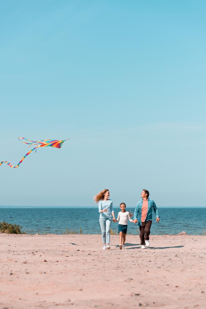 Selective focus of woman with kite walking near daughter and husband on beach  - Photo, Image