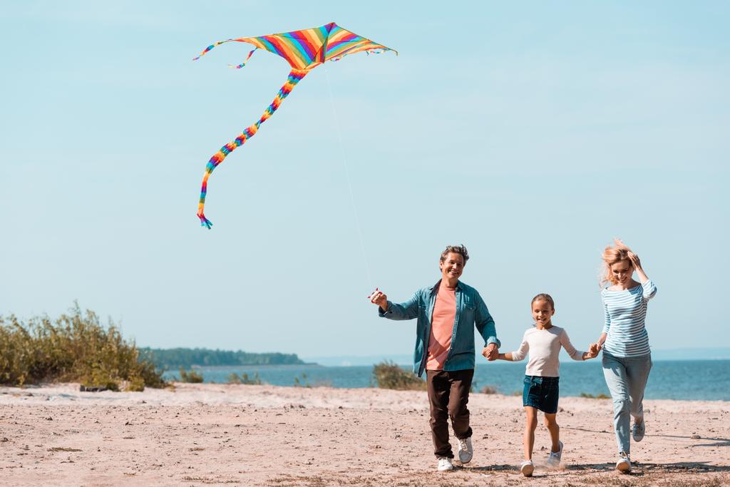 Familie mit Tochter und Drachen läuft im Urlaub am Strand  - Foto, Bild