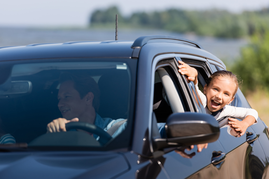 Selectieve focus van opgewonden meisje kijken door het raam van de auto in de buurt van vader  - Foto, afbeelding