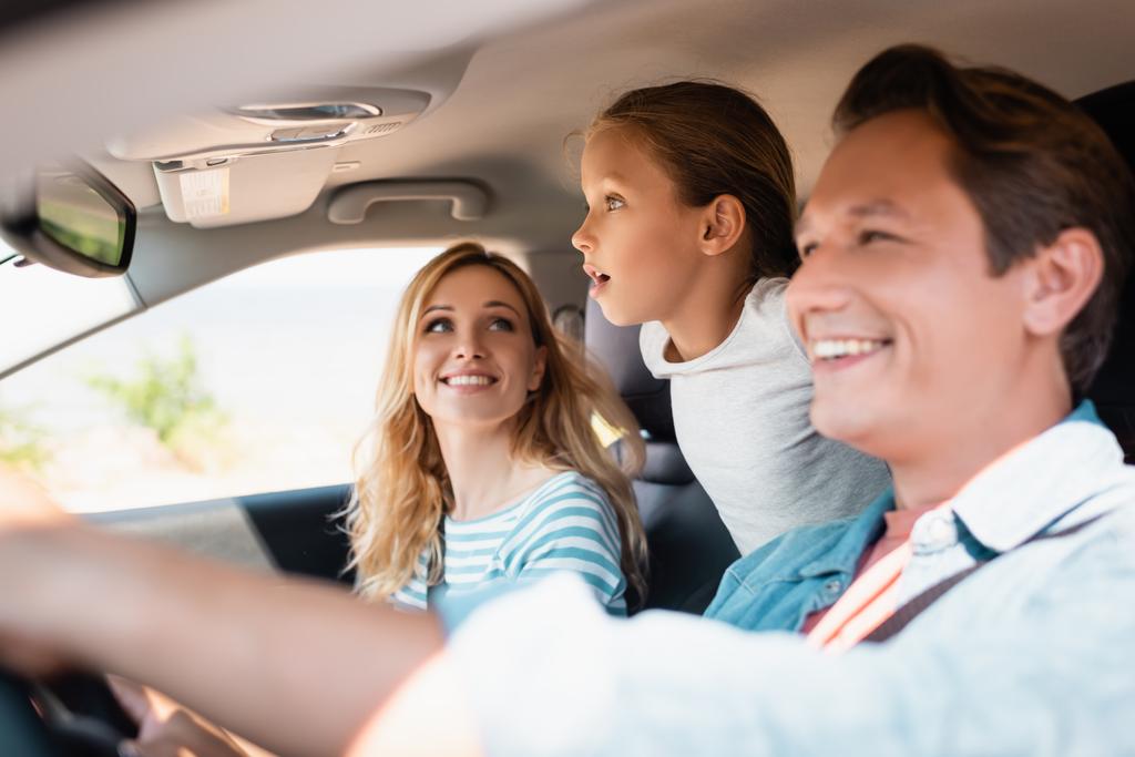 Избирательный фокус возбужденной девочки, отводящей взгляд во время поездки с родителями в машине  - Фото, изображение