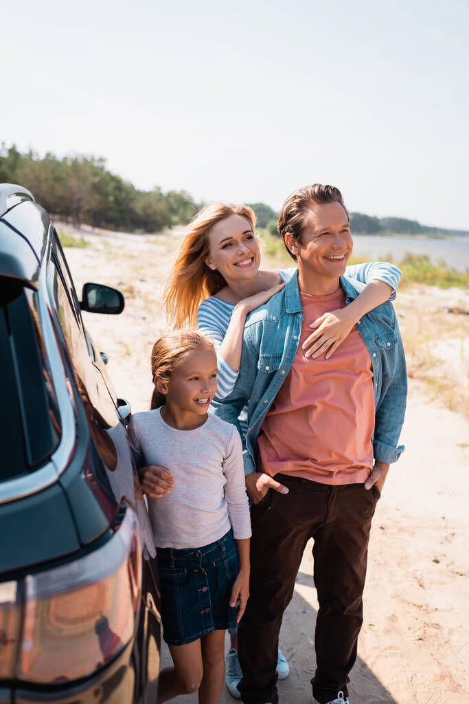 Selective focus of woman embracing husband near daughter and auto on beach  - Photo, Image