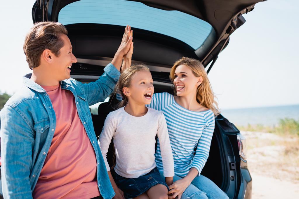 Selectieve focus van ouders geven high five in de buurt dochter en auto op het strand  - Foto, afbeelding