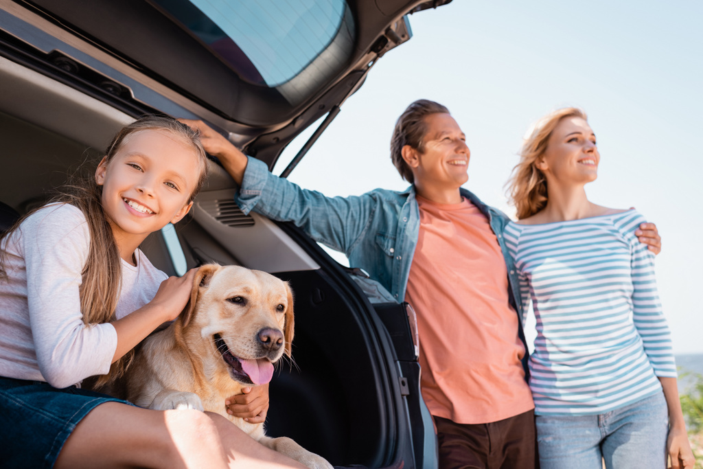 Selektywne skupienie dziewczyny pieszczoty golden retriever pobliżu rodziców obejmując obok samochodu na zewnątrz  - Zdjęcie, obraz