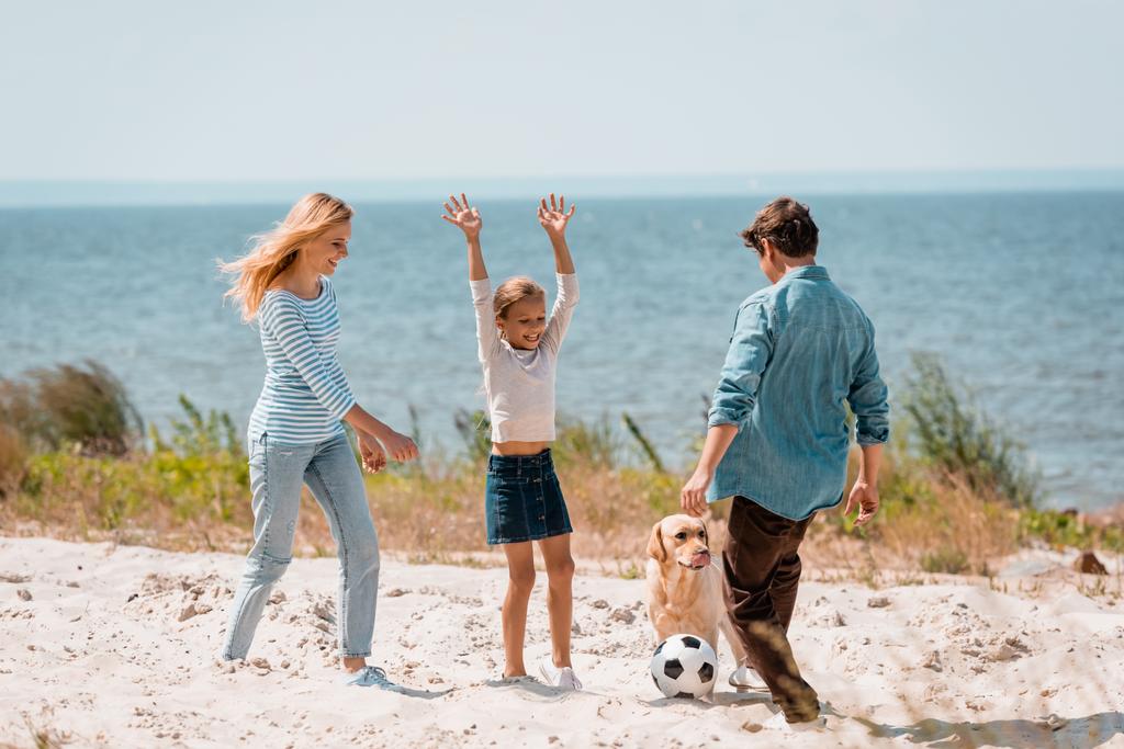 Valikoiva painopiste lapsi pelaa vanhempien kanssa jalkapallossa lähellä kultainen noutaja rannalla  - Valokuva, kuva