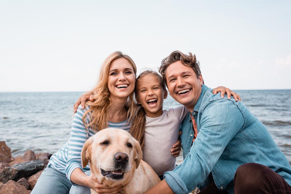 Familie mit Golden Retriever blickt am Strand in die Kamera  - Foto, Bild