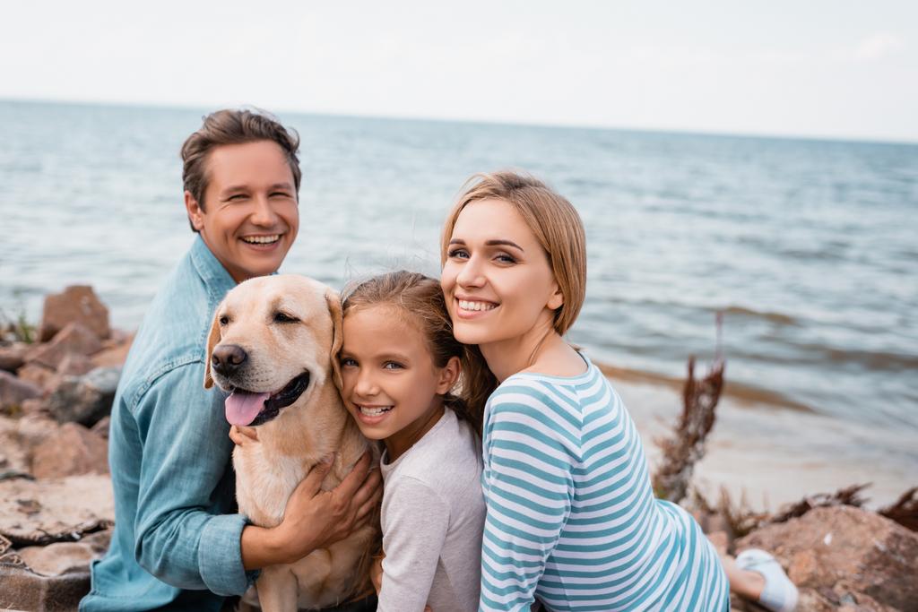 Perhe lapsi ja kultainen noutaja katselee kameraa viikonloppuna rannalla  - Valokuva, kuva