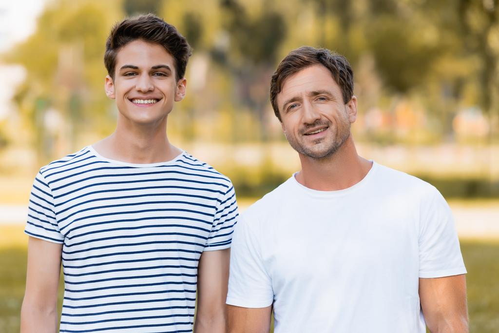 père et adolescent fils en t-shirts regardant caméra à l'extérieur - Photo, image