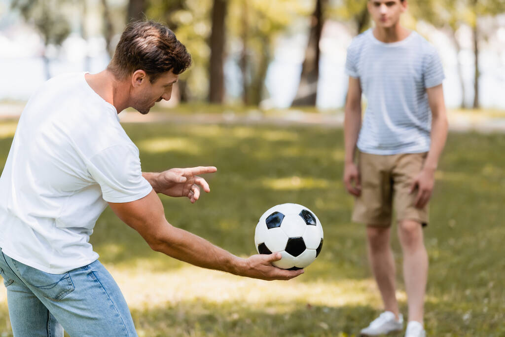 επιλεκτική εστίαση του πατέρα κρατώντας το ποδόσφαιρο στο χέρι κοντά έφηβος γιος - Φωτογραφία, εικόνα