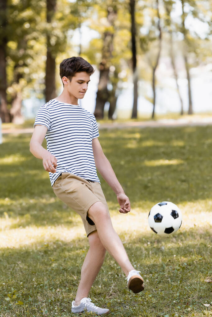Soyunmuş tişörtlü genç dışarıda futbol oynuyor.  - Fotoğraf, Görsel