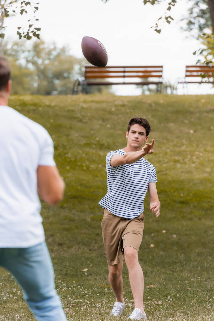 вибірковий фокус хлопчика-підлітка кидає м'яч регбі батькові в зелений парк
  - Фото, зображення
