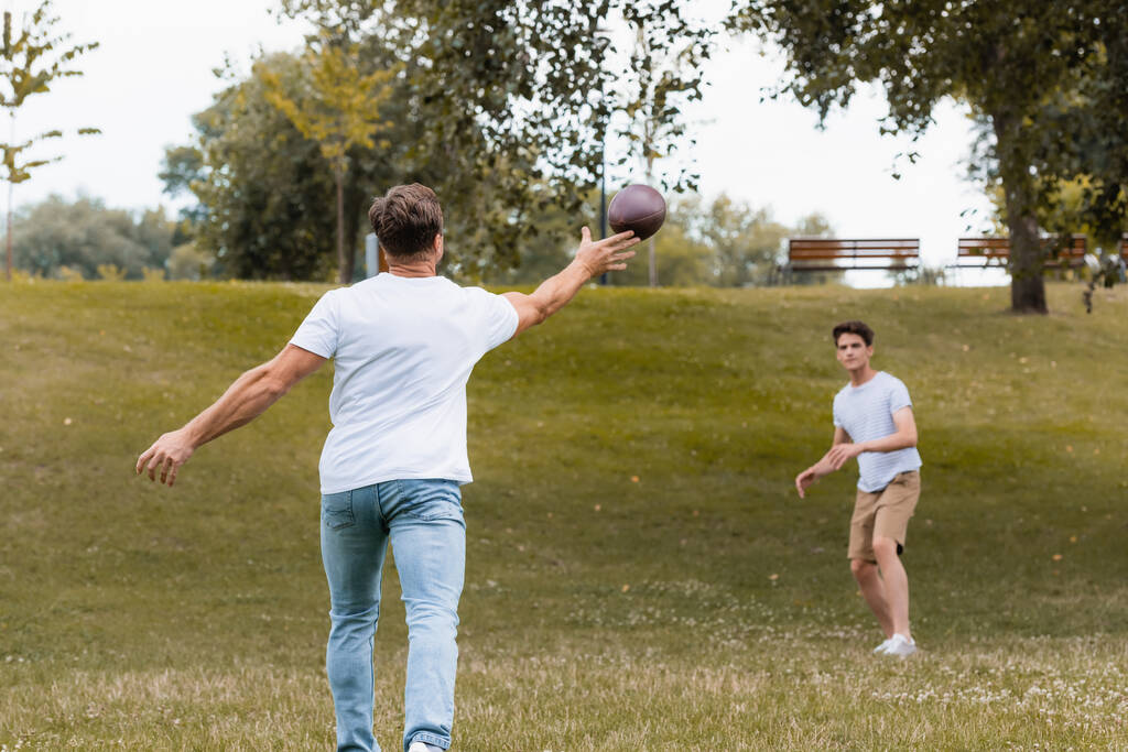 foyer sélectif de père lançant la balle de rugby au fils adolescent dans le parc vert  - Photo, image