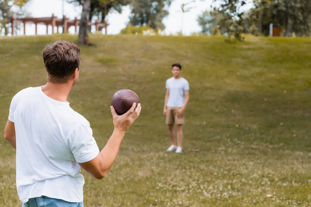 グリーンパークの10代の息子の近くでラグビーボールを持っている父親の選択的な焦点  - 写真・画像