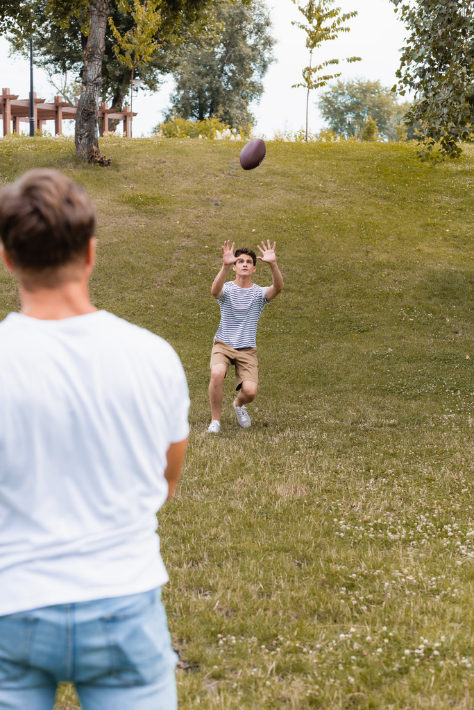 Genç oğlanın parkta babasının yanında rugby topu yakalamasına odaklanmış.  - Fotoğraf, Görsel