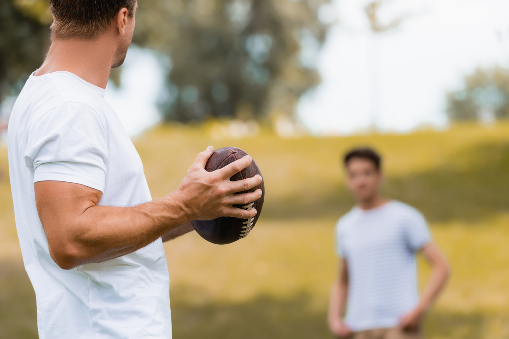selective focus of man holding rugby ball near teenager son in green park  - Photo, Image